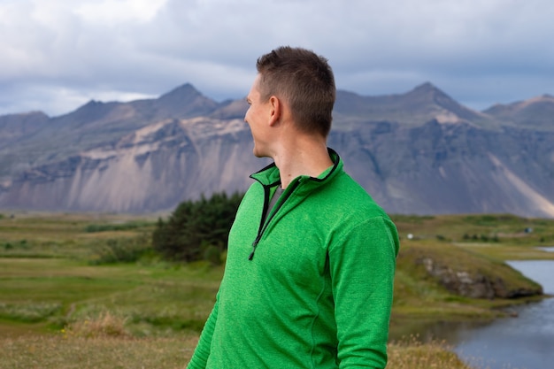 Backside of tall caucasian man wearing green jacket standing in over mountain and fog background