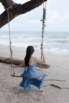 Retro della donna seduta su altalena in legno,sfondo spiaggia,modella in posa,tempo di relax