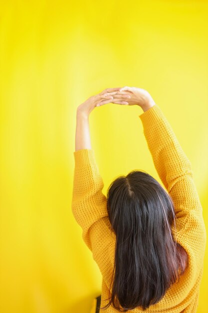 Backside of woman in sweater stretching and tilting body after
good sleep yellow background