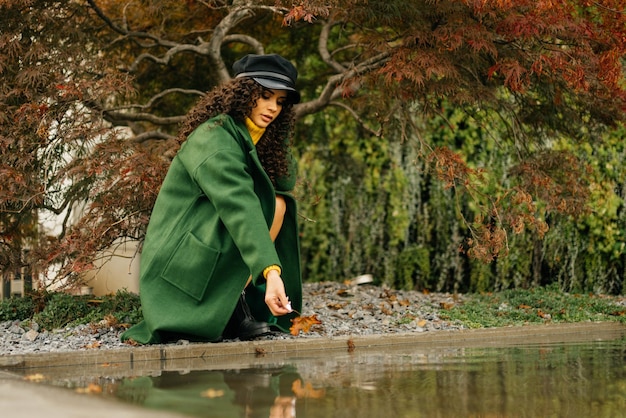 At the backwater in the park crouched girl and reaches for the water hand which holds a red sheet au