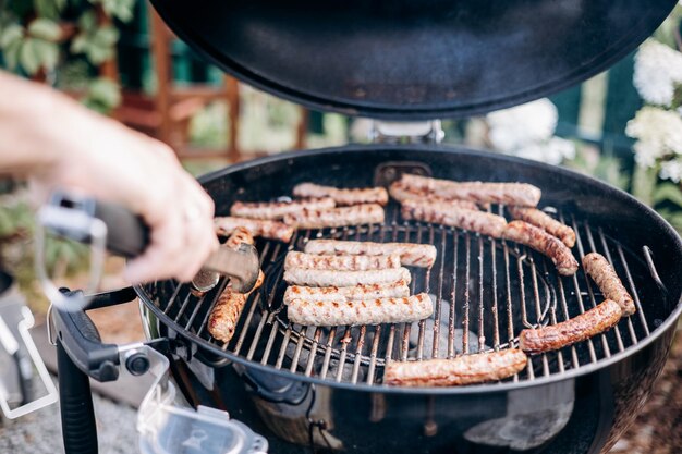 Backyard BBQ Closeup of grilling sausages of meat on barbecue Man preparing tasty sausages