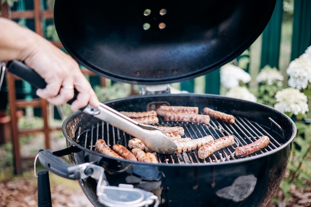 Backyard BBQ Closeup of grilling sausages of meat on barbecue Man preparing tasty sausages