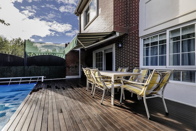 Photo backyard of a detached house with french windows with swimming pool covered by a blue protective tarp acacia wood floors metal perimeter fence dining table with matching chairs