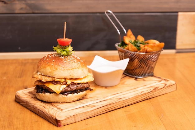 bacon burguer with french fries and sauce over a wooden table