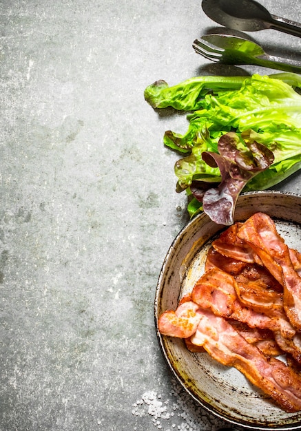 Bacon in a frying pan with salt and herbs. On a stone background.