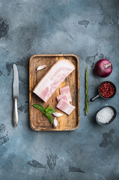 Pancetta pancetta tagliata e affettata con erbe su sfondo grigio testurizzato, vista dall'alto.