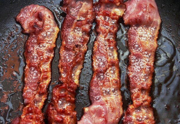 Bacon slice being cooked in frying pan