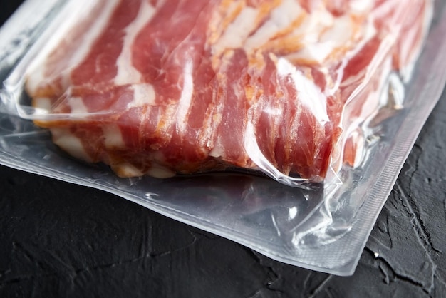 Bacon strips rauwe gerookte varkensvlees plakjes in vacuümverpakking op zwarte tafel