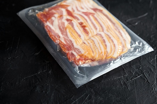 Photo bacon strips raw smoked pork meat slices in vacuum package on black table