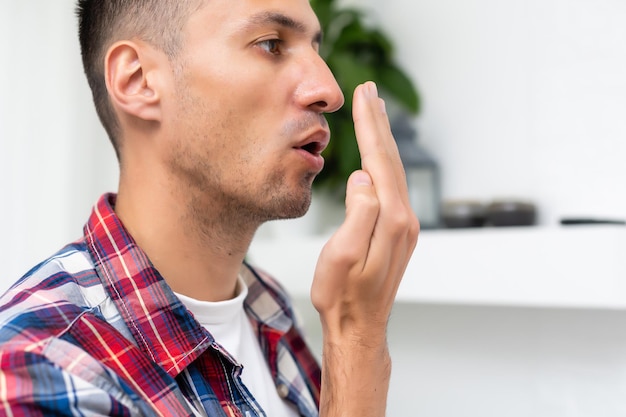 Bad breath. Halitosis concept. Young man checking his breath with his hand.