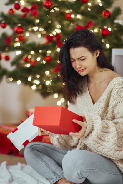 家で屋内でプレゼントボックスを開いた失望と不幸な女性の悪いクリスマスプレゼント