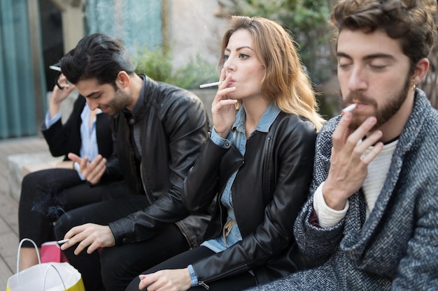 Bad habits - group of young friends smoking cigarettes together outdoors. Unhealthy addiction concept.