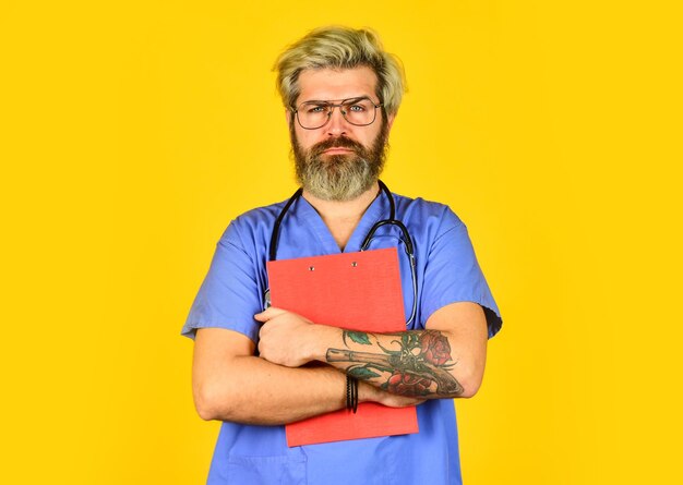 Bad news nurse holding binder and wearing stethoscope mature bearded male doctor with a folder in uniform standing portrait of serious nurse with a folder he is wearing a stethoscope