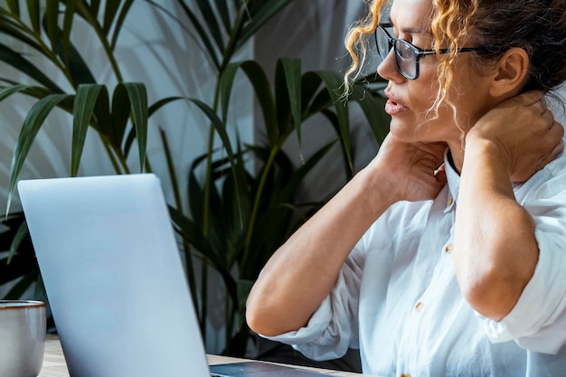 Bad posture back neck ache and tired expression One woman massaging her body after long work Overwork Close up portrait of small business entrepreneur wearing eyewear and using laptop computer