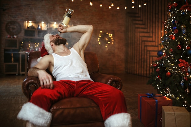 Bad Santa claus with bottle of alcohol sitting on couch