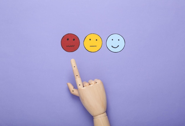 bad service customer satisfaction survey concept hand chooses sad face icon happy neutral face paper icon on violet background top view