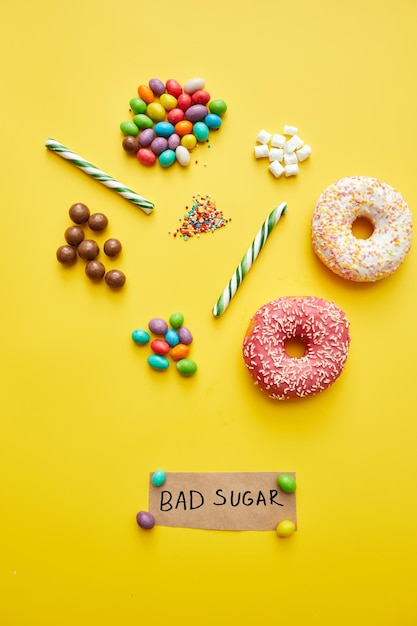 Photo bad sugar concept various unhealthy sweets such as doughnuts jellybeans and candy canes on yellow ba