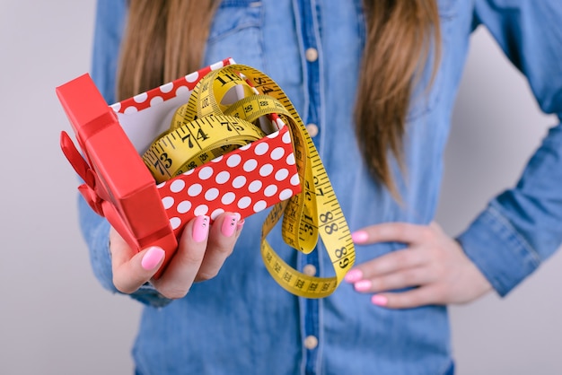 Bad unwanted unwished gift for people lady person concept. Cropped closeup photo of disappointed confused frustrated student holding showing tape measure in hand isolated grey background