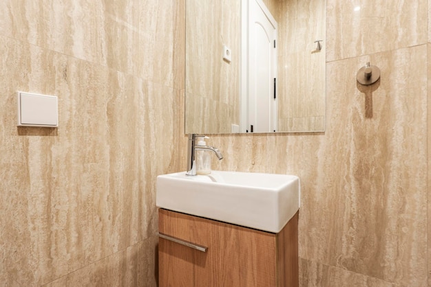 Badkamer met frameloze vierkante spiegel witte porseleinen wastafel op houten kast en crème marmeren tegels