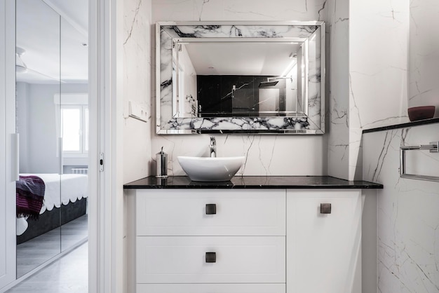 Badkamer met houten meubels met witte laden, zwart marmeren aanrechtblad en plank met metalen en glazen frame