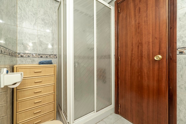 Badkamer met vierkante douchecabine met wit scherm en rieten ladeblok