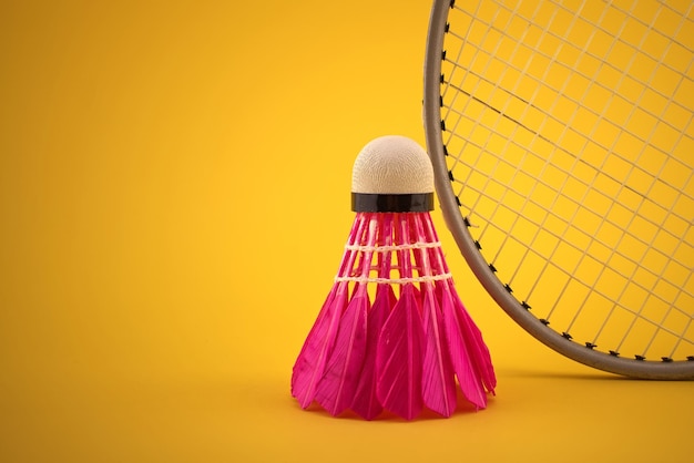 Photo badminton feather shuttlecock near badminton racket over a yellow background with copy space