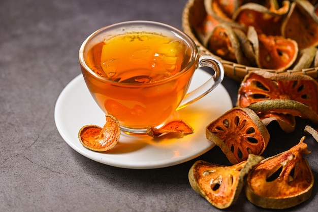 Bael tea on glass with dried bael slices on dark background Bael juice Dry bael fruit tea for health Aegle marmelos