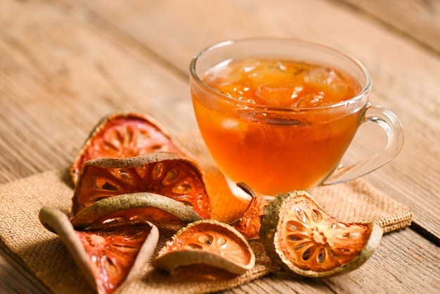 Bael tea on glass with dried bael slices on wooden background Bael juice Dry bael fruit tea for health Aegle marmelos