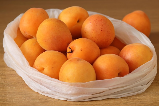 A bag of apricots is on a table with a wooden surface.