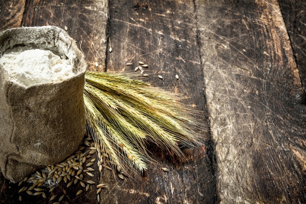 Мешок муки и колоски пшеницы на деревянном фоне