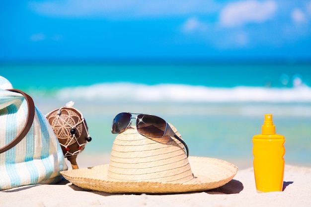 Bag, maracas, straw hat with sunglasses and sunscreen lotion bottle on white sand