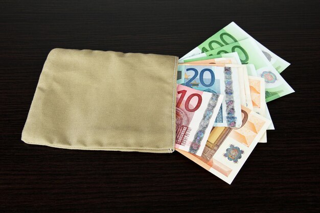木製の背景に異なるユーロ紙幣とお金の袋