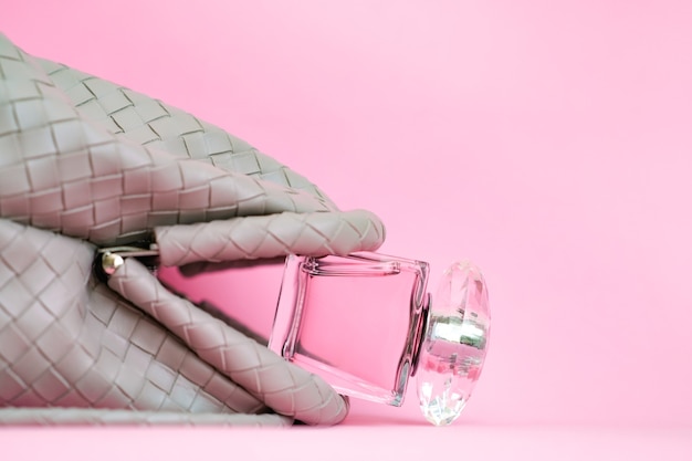 Bag on a pink background. A bottle of perfume falls out of a womans purse