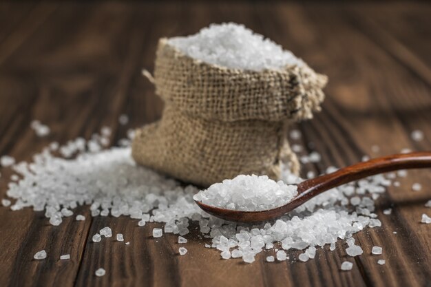 A Bag Of Salt And A Wooden Spoon On A Rustic Table. Ground Stone Sea Salt.