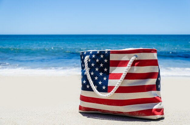 Foto borsa con i colori della bandiera americana vicino oceano sulla spiaggia di sabbia