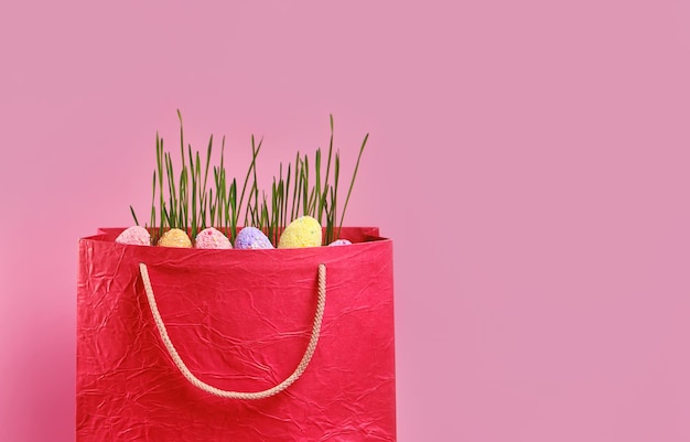 Bag with grass Easter eggs on pink background