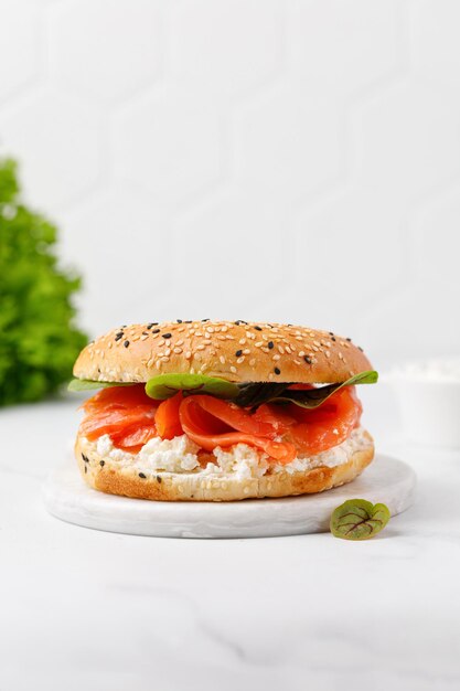 Bagel sandwich with salmon cream cheese and green leaves on marble board and white background Burger