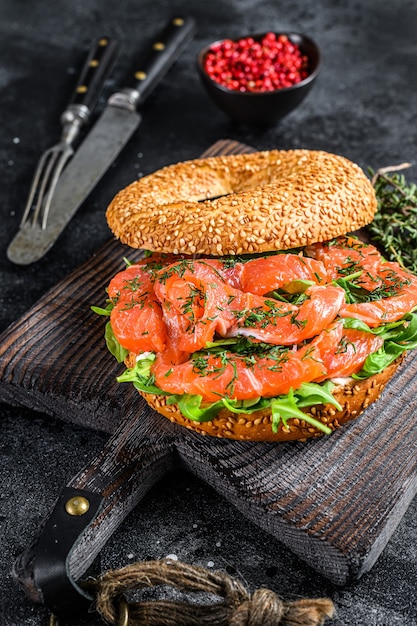 Bagel van gerookte zalm met zachte kaas, rucola op een houten snijplank. Zwarte achtergrond. Bovenaanzicht.