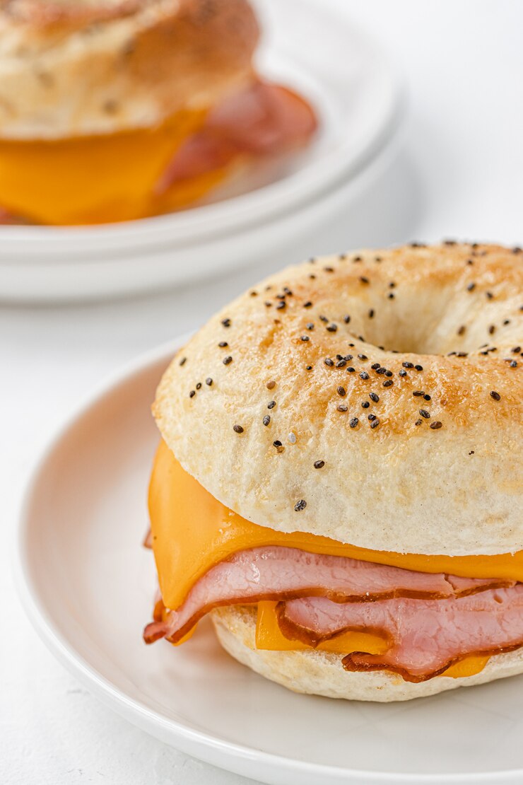 Photo bagel with ham and cheddar cheese on white plate