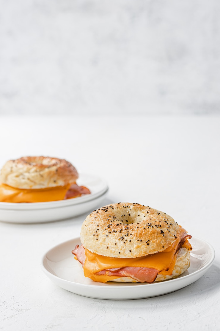 Photo bagel with ham and cheddar cheese on white plate