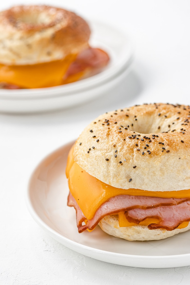 Photo bagel with ham and cheddar cheese on white plate