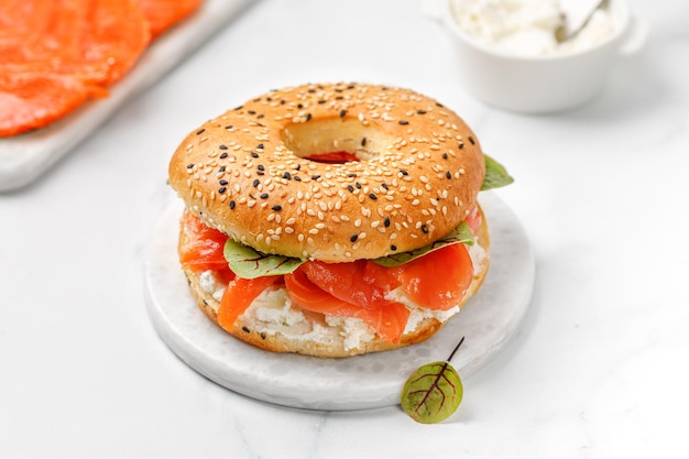 Bagel with salmon cream cheese and micro greens on board and marble background