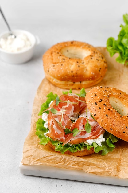 Bagels met ham prosciutto roomkaas letucce microgreens op papier en grijze achtergrond