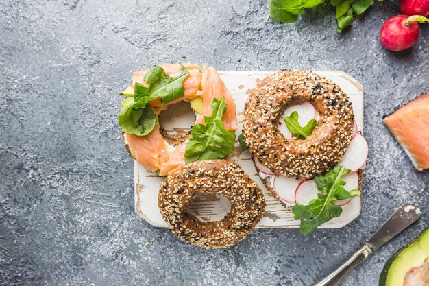 Bagels with cream cheese avocado, fish, arugula and radish. Healthy breakfast food. Top view.