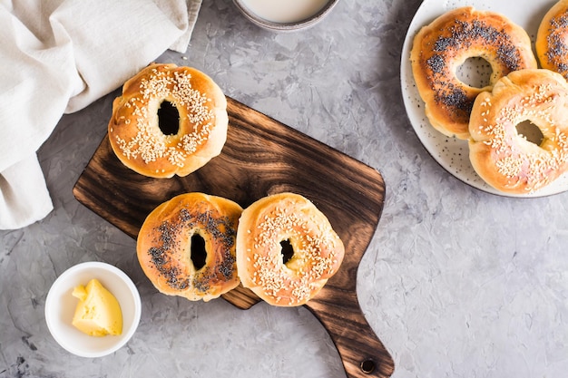 Bagels with poppy seeds and sesame on the board and butter in a bowl on the table Top view