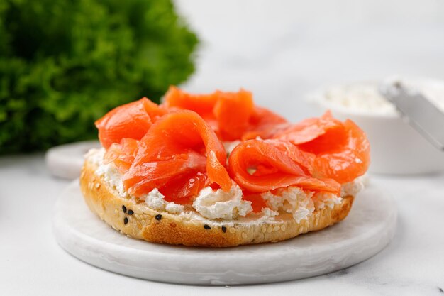 Bagelsandwich met zalm en roomkaas op marmeren bord en witte achtergrond