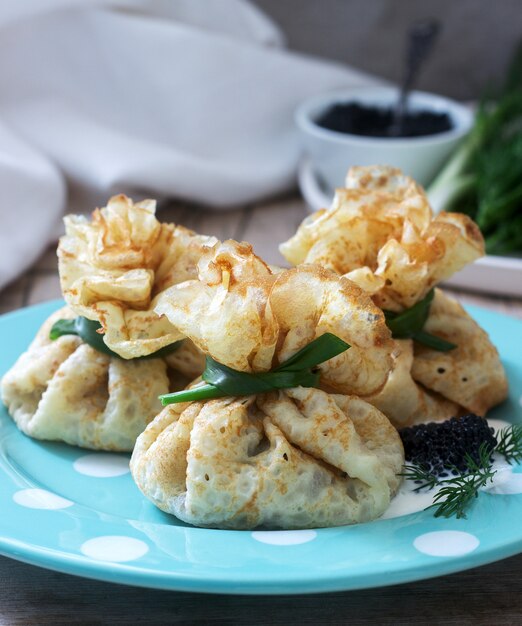 Bags of pancakes stuffed with herring, served with caviar, sour cream and dill on a wooden background. Rustic style.