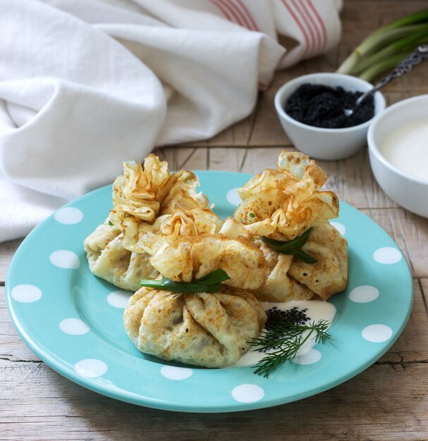 Foto sacchetti di pancake ripieni di aringhe, servito con caviale, panna acida e aneto su un fondo di legno. stile rustico.