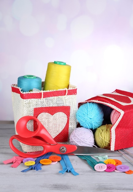 Bags with bobbins of colorful thread and woolen balls on wooden table on light background