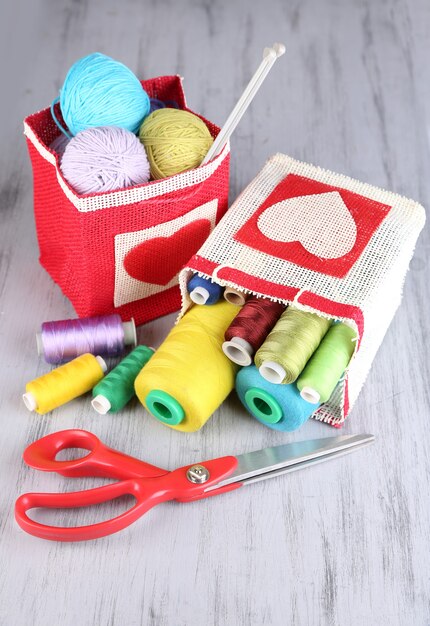 Bags with bobbins of colorful thread and woolen balls on wooden